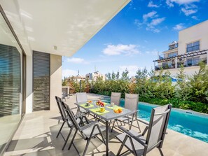 A patio with a table and chairs, a pool, and surrounding greenery. - Azure Seaview - Garnet Villa (Paralimni)