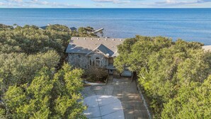 A stone house with a paved driveway and a dock extending into a body of water. - Soundfront Dog Friendly w/ Hot Tub, Elevator, Private Sound Access, Media Room (Buxton)