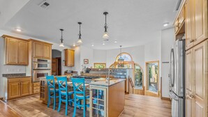 A spacious kitchen with wooden cabinets, a central island with bar stools, and a large refrigerator. - Soundfront Dog Friendly w/ Hot Tub, Elevator, Private Sound Access, Media Room (Buxton)