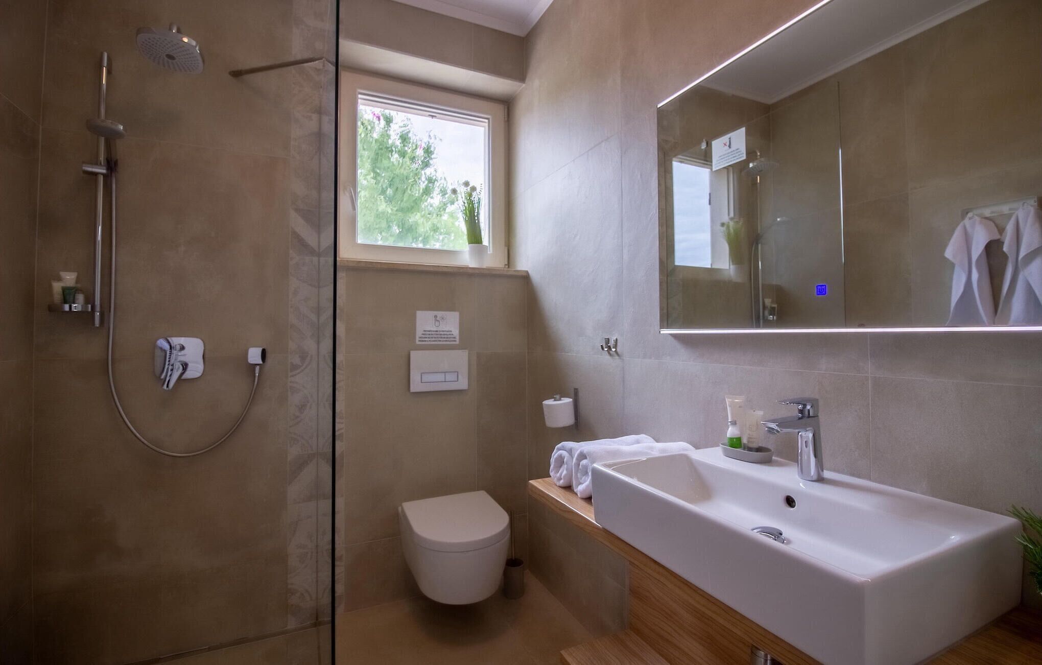 Een moderne badkamer met douche, toilet, wastafel en een grote spiegel.