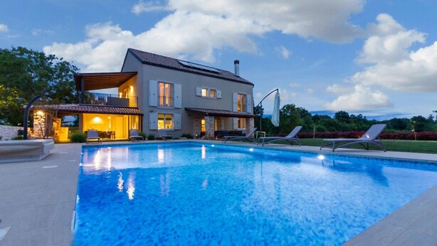 A modern two-story house with a swimming pool, outdoor seating, and a view of the landscape.