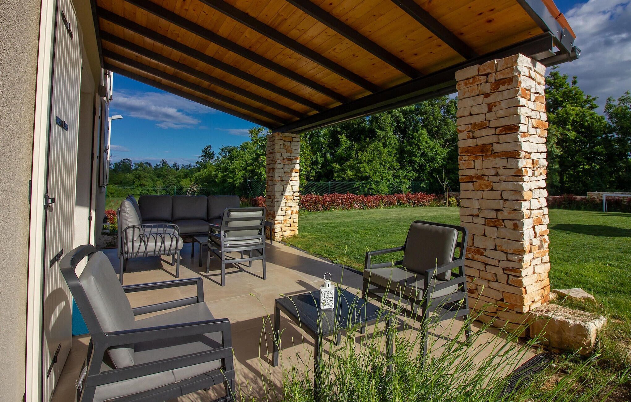 An outdoor patio with a wooden pergola, stone pillars, and a sectional sofa.
