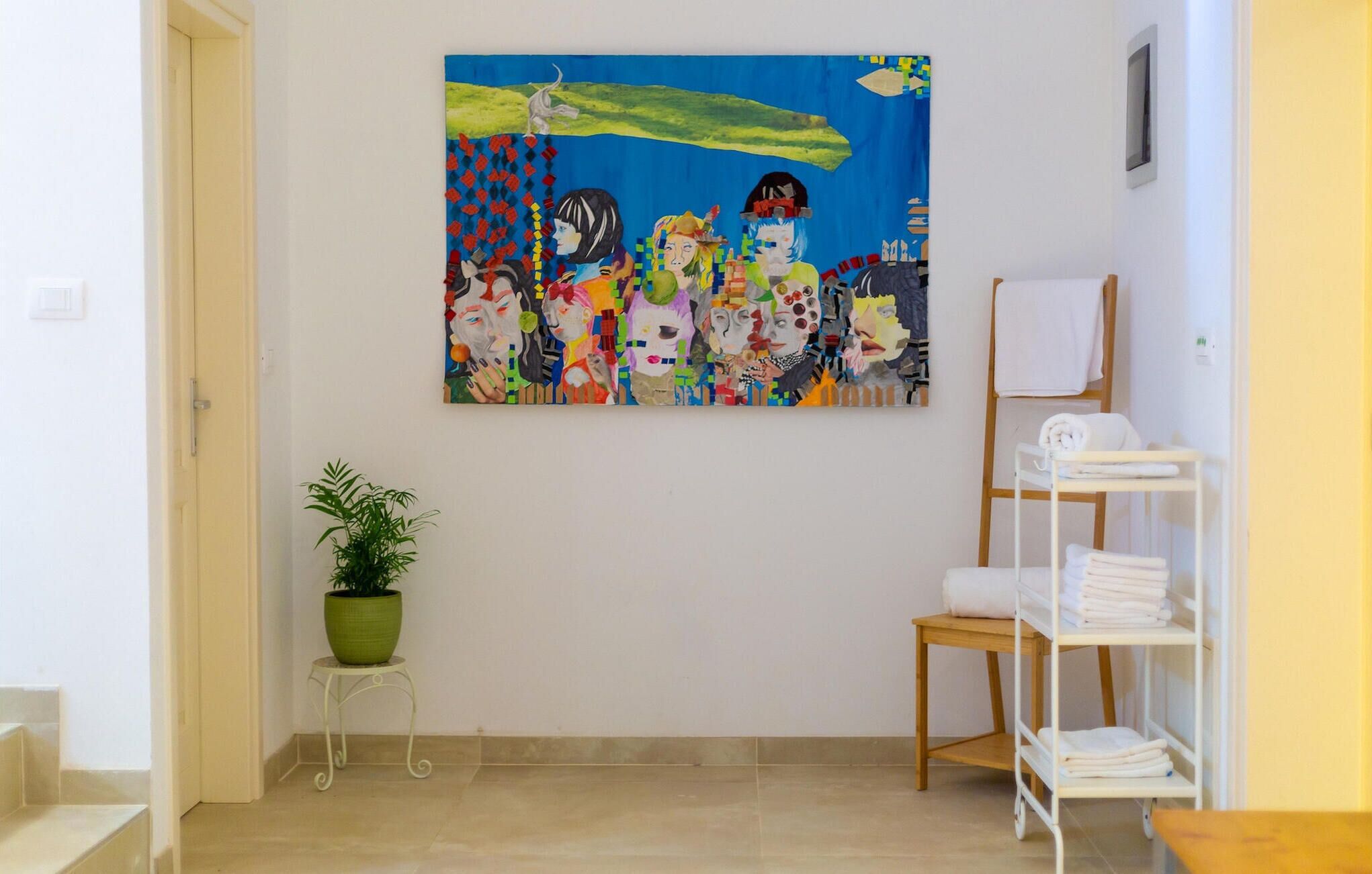 A hallway with a large abstract painting, a potted plant, a white shelf with towels, and a wooden chair.