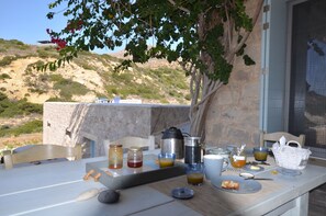 A breakfast table set outdoors with a stone wall and a view of hills.