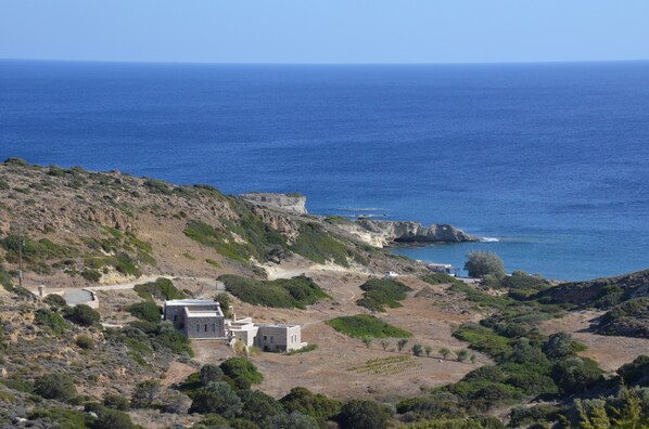 A coastal landscape with rocky terrain, a small building with a stone facade, and the sea in the background.