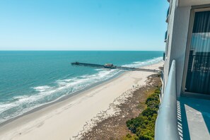 Vista de una playa con un muelle que se adentra en el océano, una playa arenosa y un edificio con balcón que domina la escena.