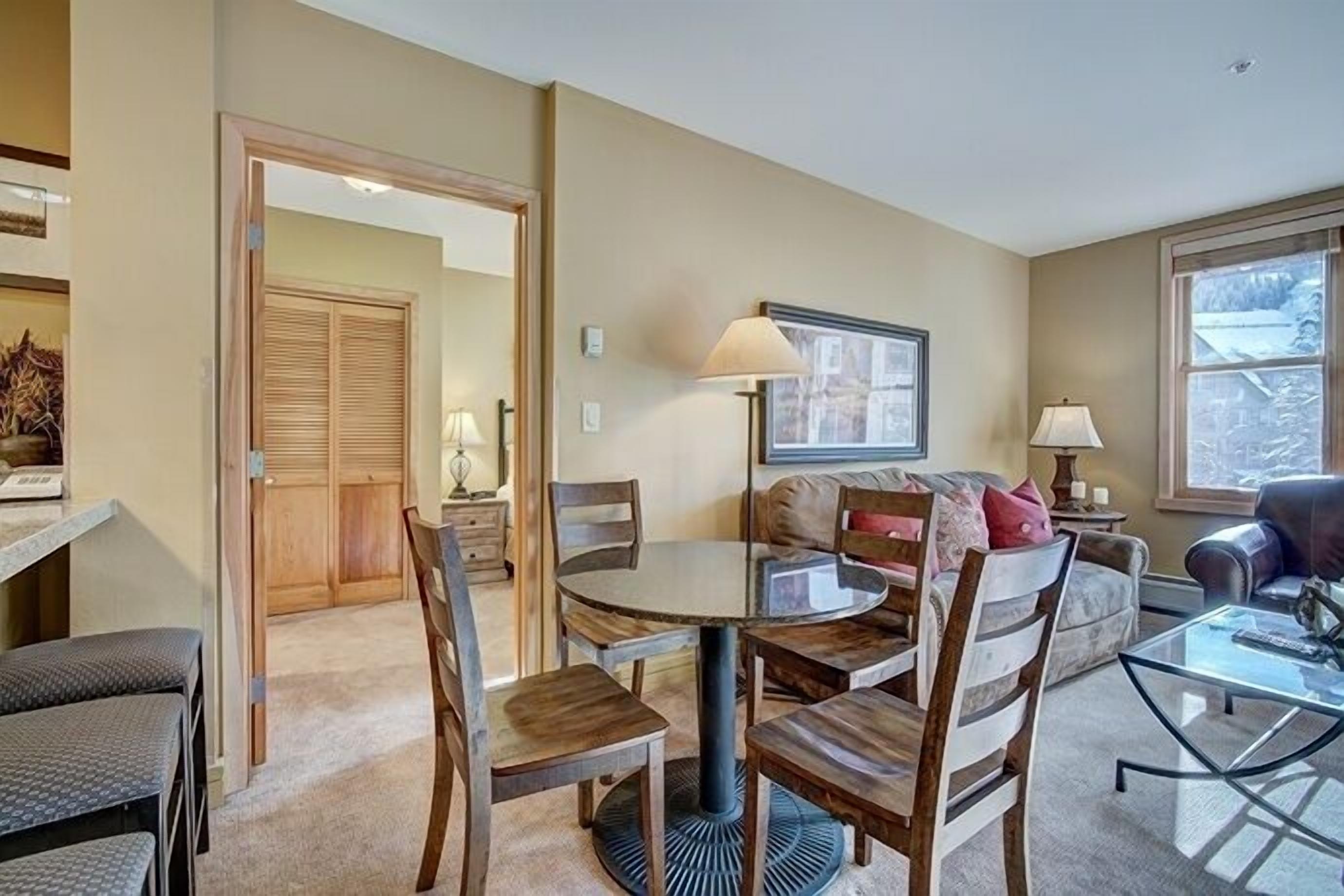 A cozy living room with a round dining table, wooden chairs, a sofa, and a glass coffee table.