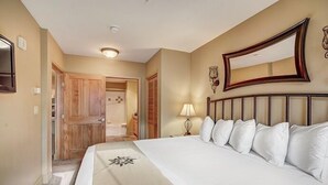Une chambre d’hôtel avec un grand lit, une armoire en bois, un miroir et une lampe.