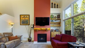A living room with a fireplace, a television mounted above it, and a large window offering a view of trees. - 1849 The Seasons 3 Bedroom Townhouse by RedAwning (Keystone)