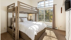 A bunk bed with a ladder, a bedside table with a lamp, a large window with curtains, and a flat-screen TV mounted on the wall. - 1849 The Seasons 3 Bedroom Townhouse by RedAwning (Keystone)