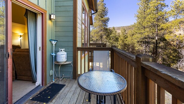 A wooden deck with a glass table and chairs, a door leading to a room with a bed, and a view of trees and hills. - 1849 The Seasons 3 Bedroom Townhouse by RedAwning (Keystone)