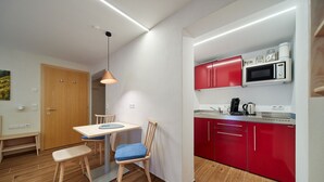 A compact kitchen with a dining area, featuring a microwave, red cabinets, and a wooden dining table with chairs. - 5003 Alice im Alpenhaus Montafon (Gargellen)