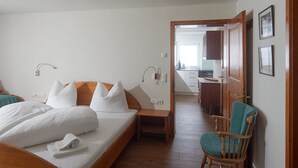 Habitación de hotel con cama, mesita de noche, silla y vista al área de la cocina.