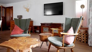 Una sala de estar con dos sillones verdes, una mesa de centro de madera, un televisor montado en la pared y un mueble de madera.