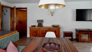 Un comedor con una mesa de madera, una lámpara colgante blanca y un televisor montado en la pared.