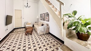 Un salon avec un sol à motifs, un canapé, une table basse, un téléviseur, un lustre, un escalier et une plante en pot.
