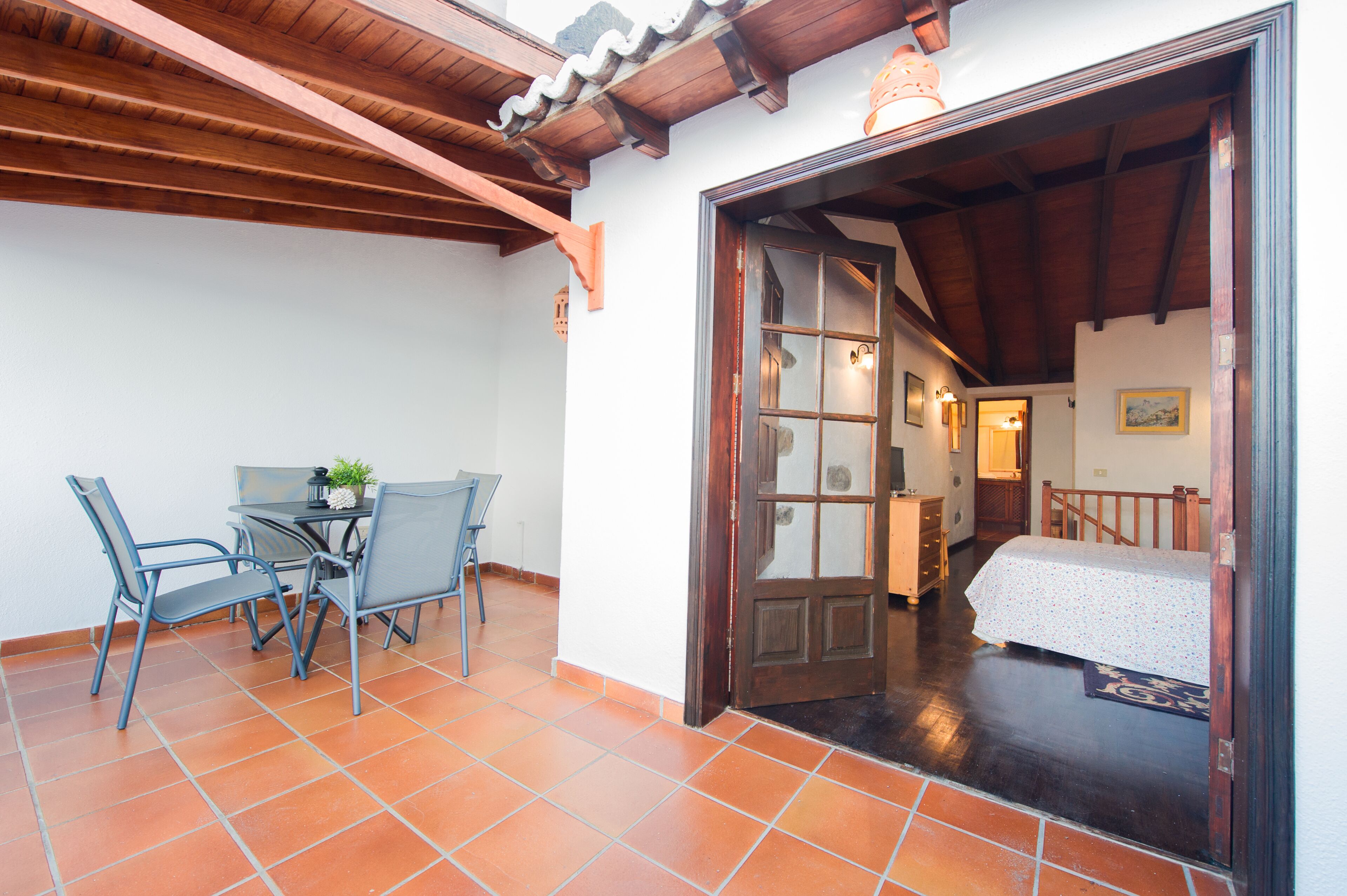 Quarto com cama, teto de madeira, chão de azulejos e porta para outro cômodo.