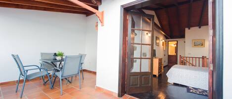 Quarto com cama, teto de madeira, chão de azulejos e porta para outro cômodo.