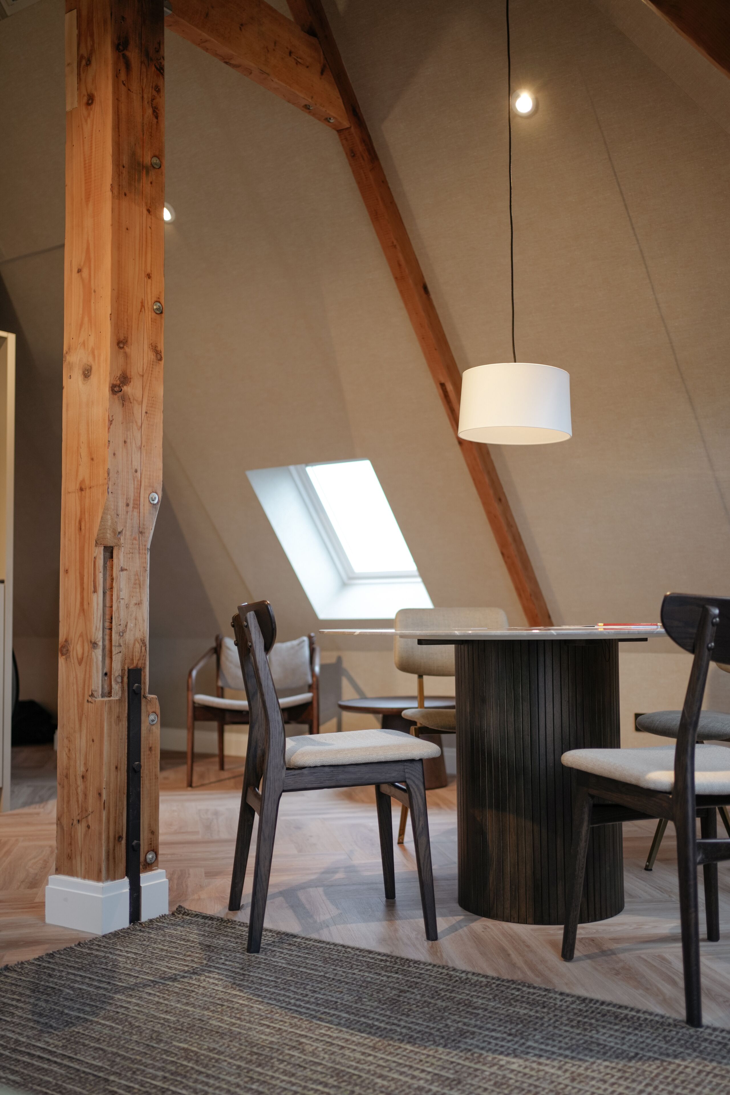 A modern loft with exposed wooden beams, a skylight, and a central table with chairs.