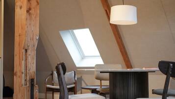 A modern loft with exposed wooden beams, a skylight, and a central table with chairs.