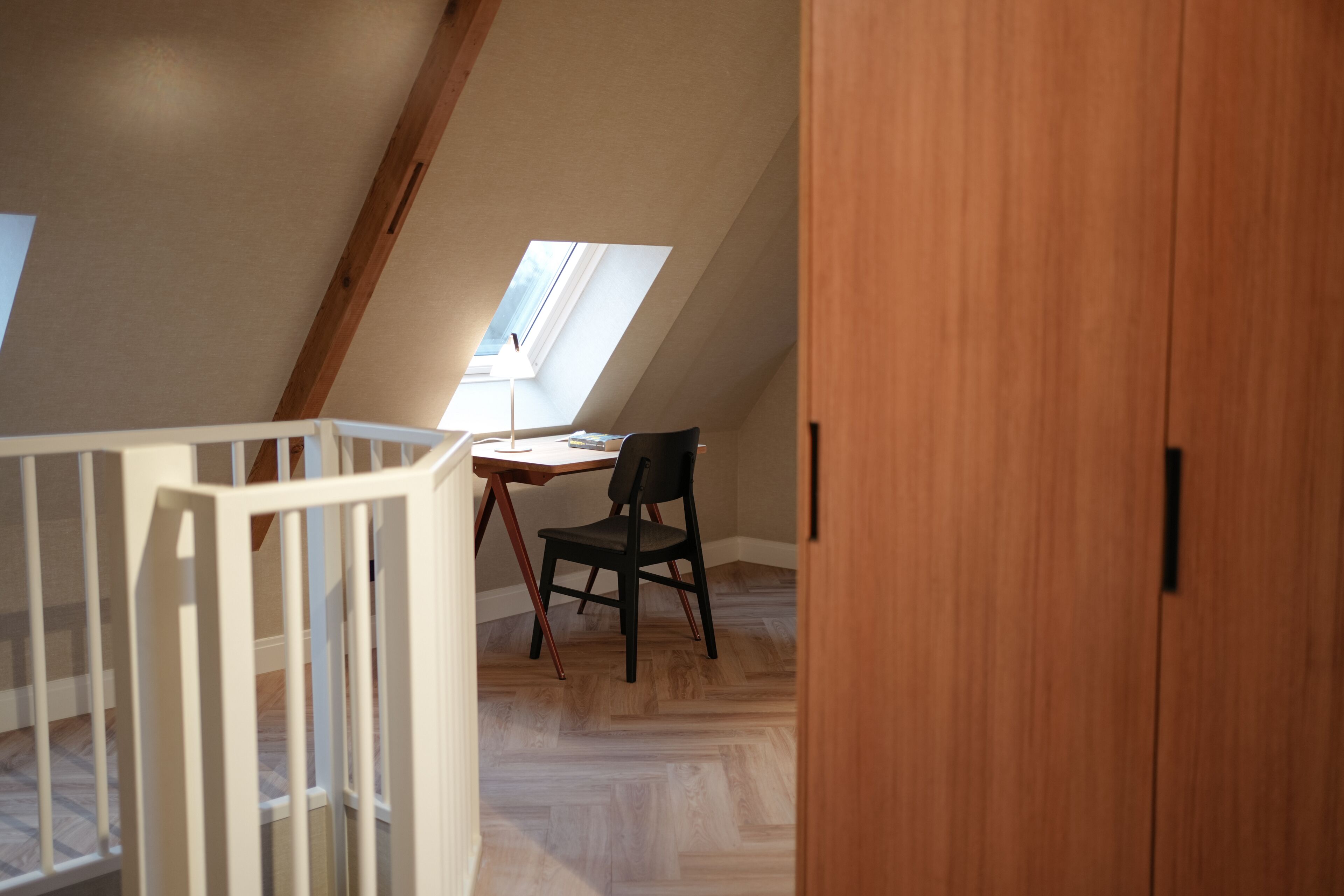 Un dormitorio en el ático con techo inclinado, un escritorio con silla y un armario de madera.
