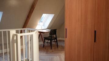 Un dormitorio en el ático con techo inclinado, un escritorio con silla y un armario de madera.