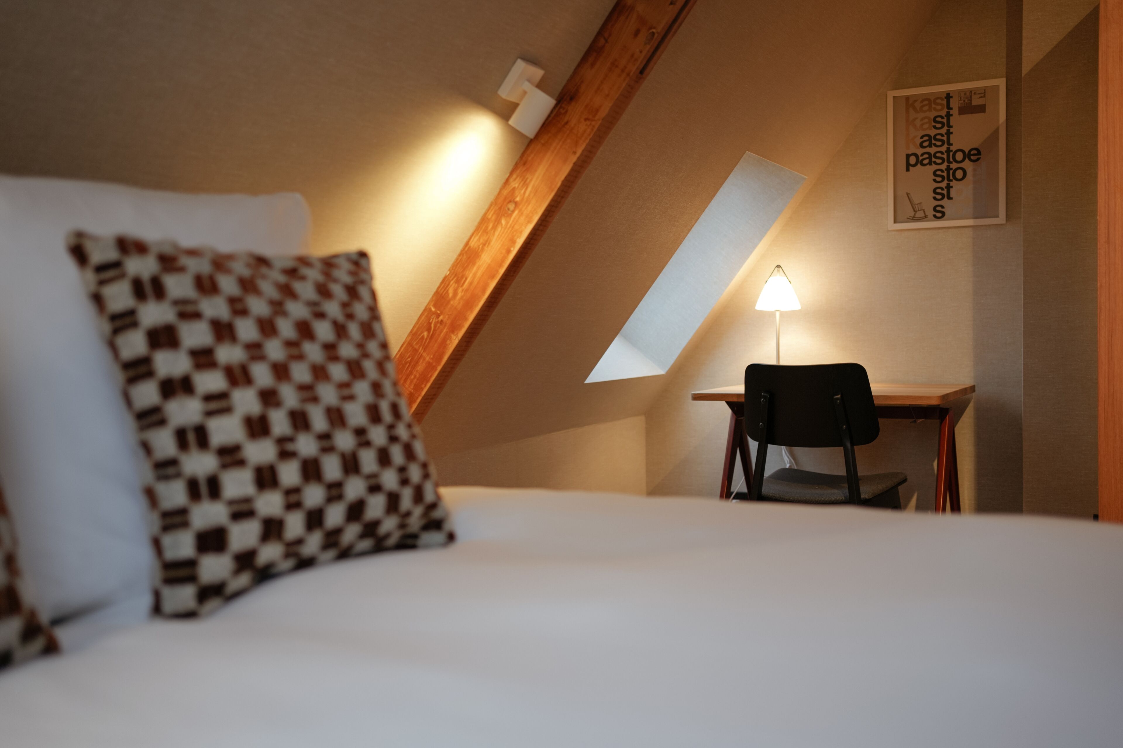 A bedroom with a bed, a desk, and a chair. There is a lamp on the desk.