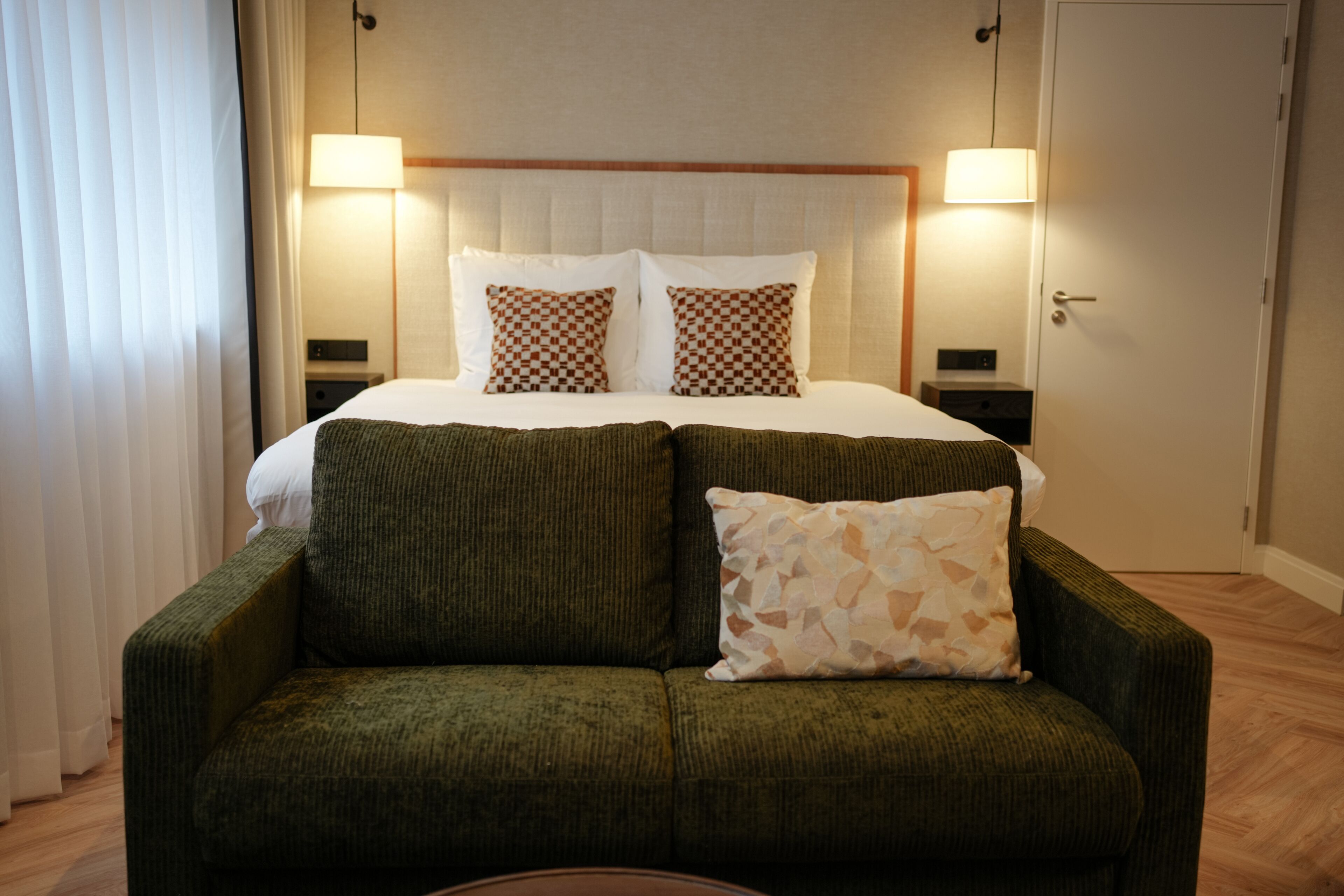 Ein Hotelzimmer mit einem Bett, zwei Nachttischlampen, einem grünen Sessel und einer Tür.