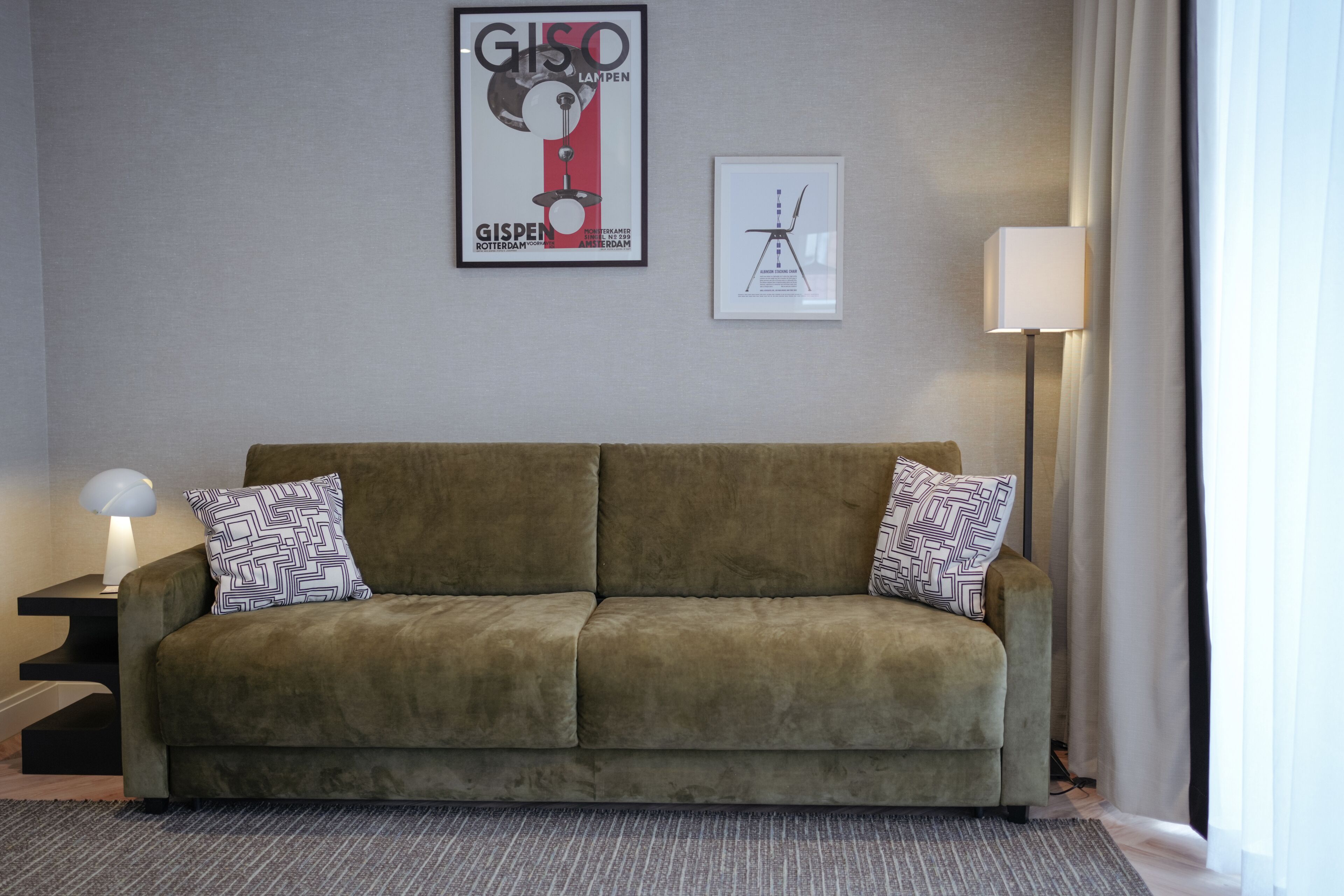 Una sala de estar con un sofá, dos almohadones estampados, un cartel enmarcado, una lámpara de pie y una mesita auxiliar.
