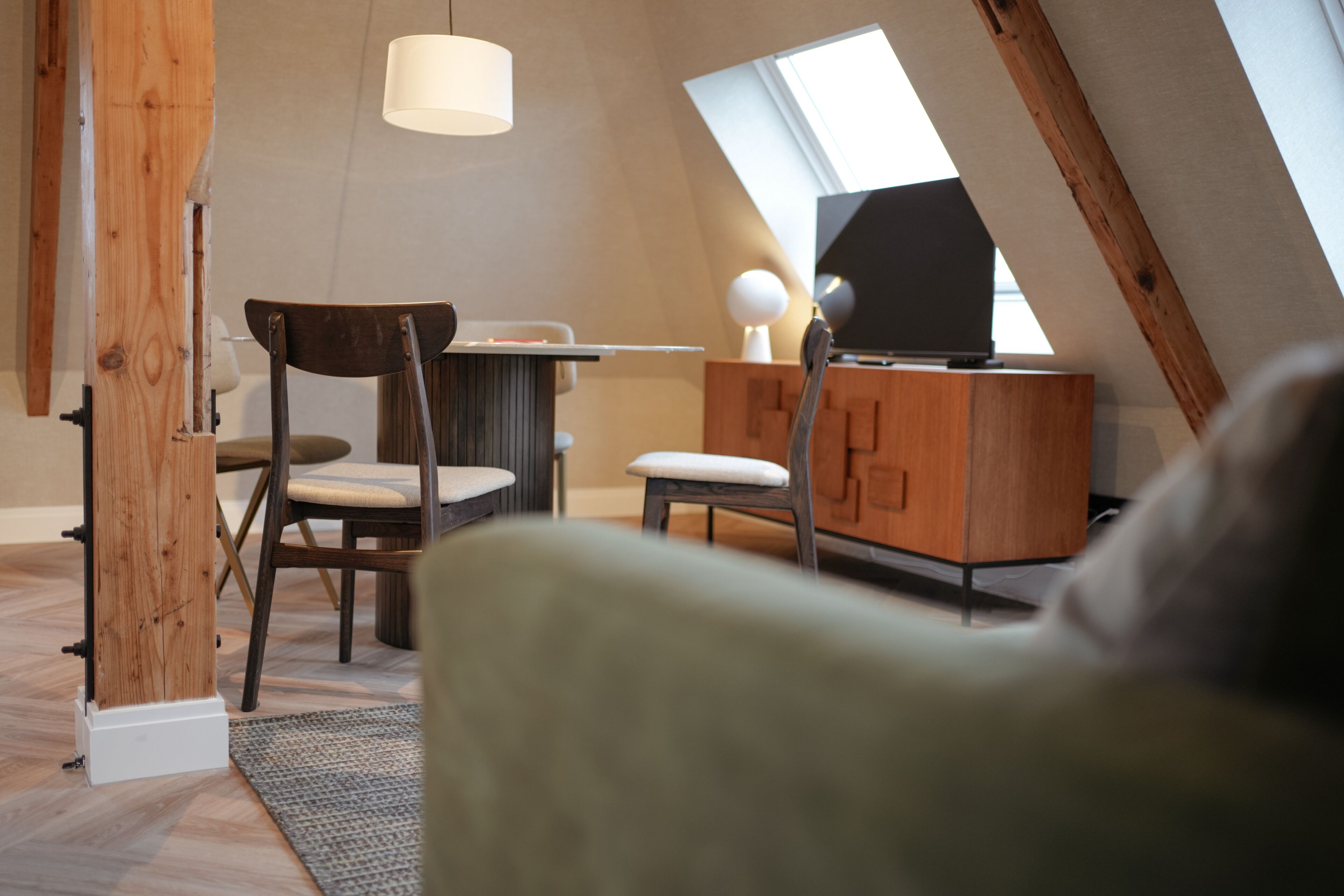 A cozy loft bedroom with a sloped ceiling, wooden beams, a desk, a chair, and a television.