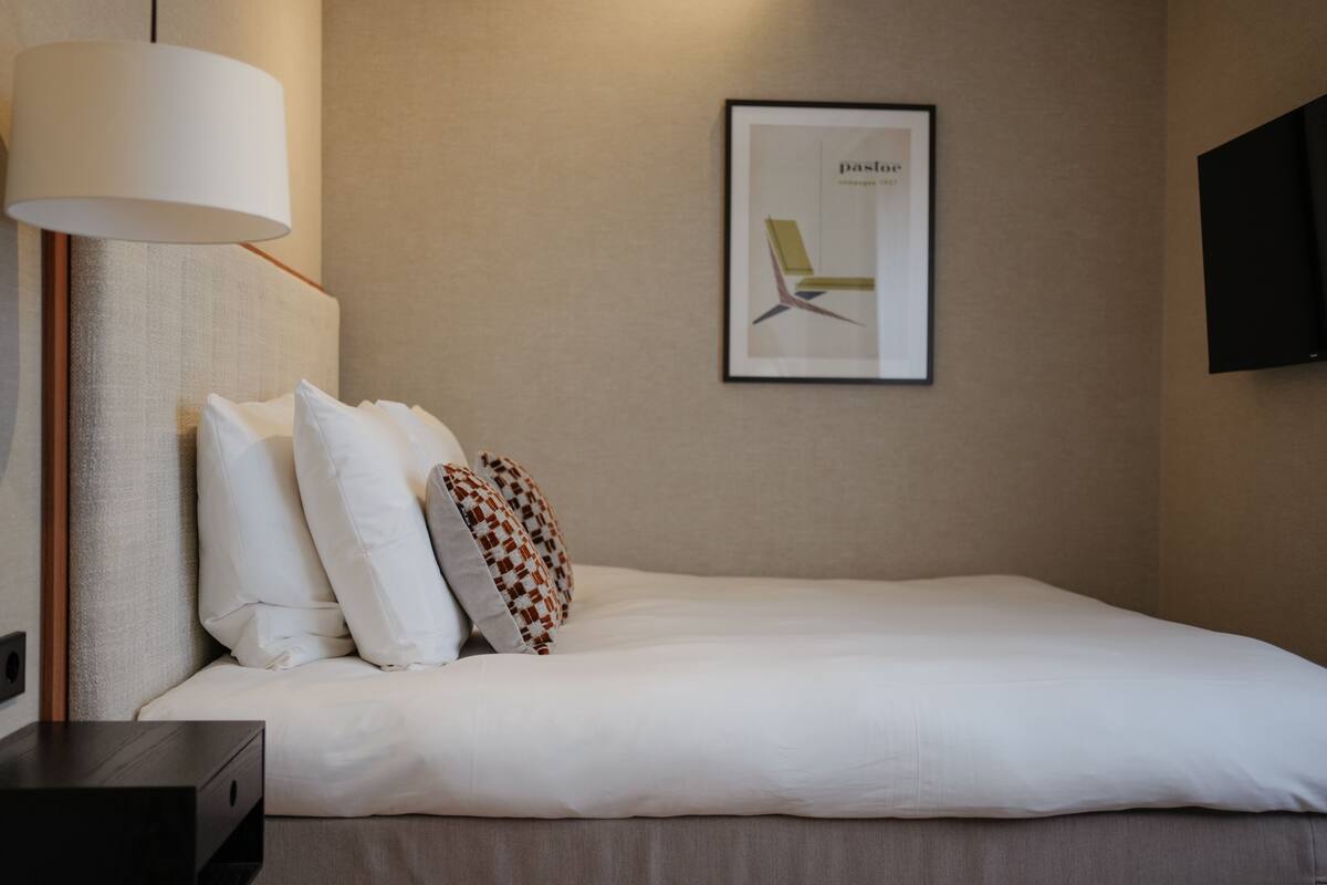 A neatly made bed with white linens, a bedside lamp, and a framed picture on the wall.