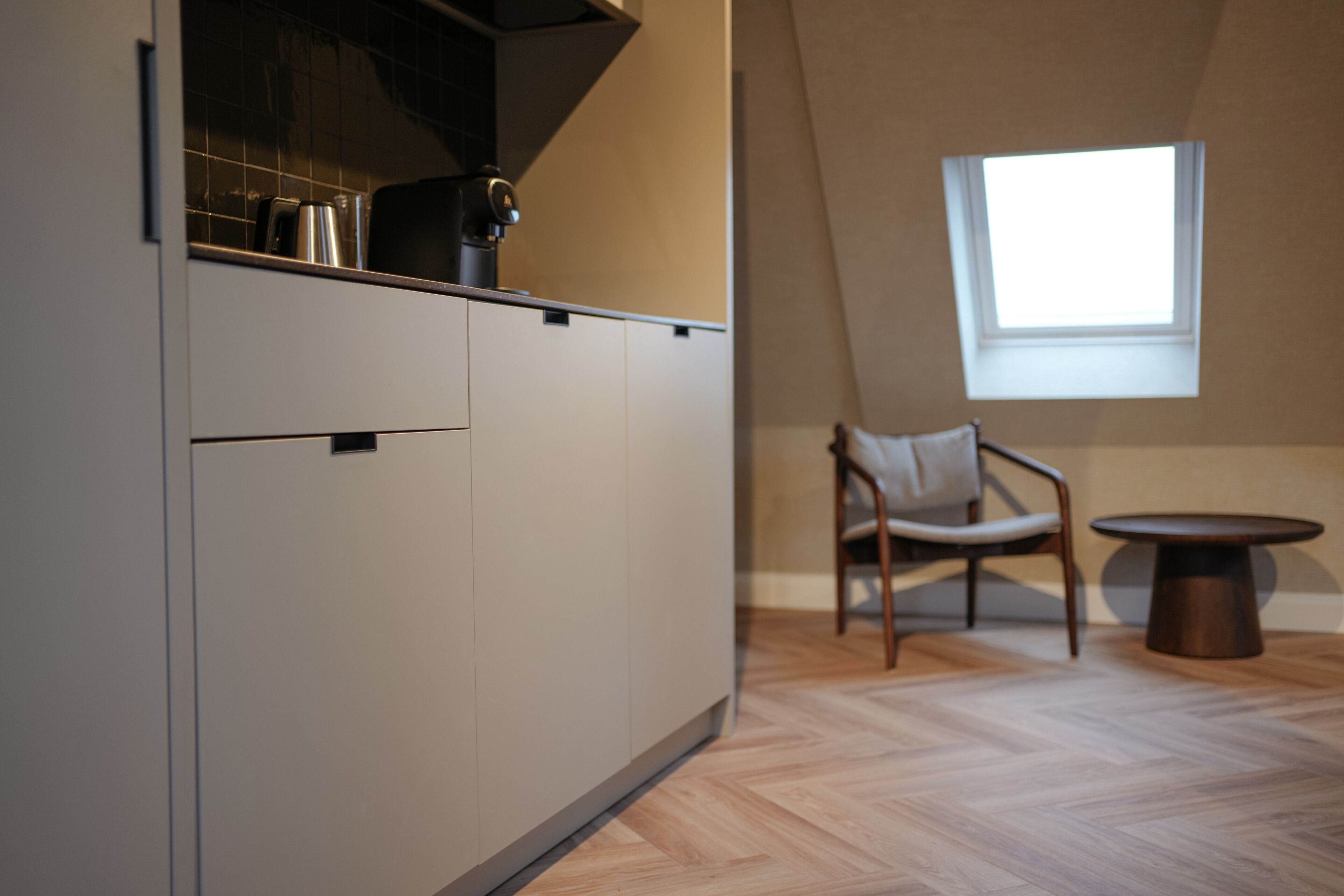 A modern kitchen with a built-in stove, a window, and a dining area with a chair and table.