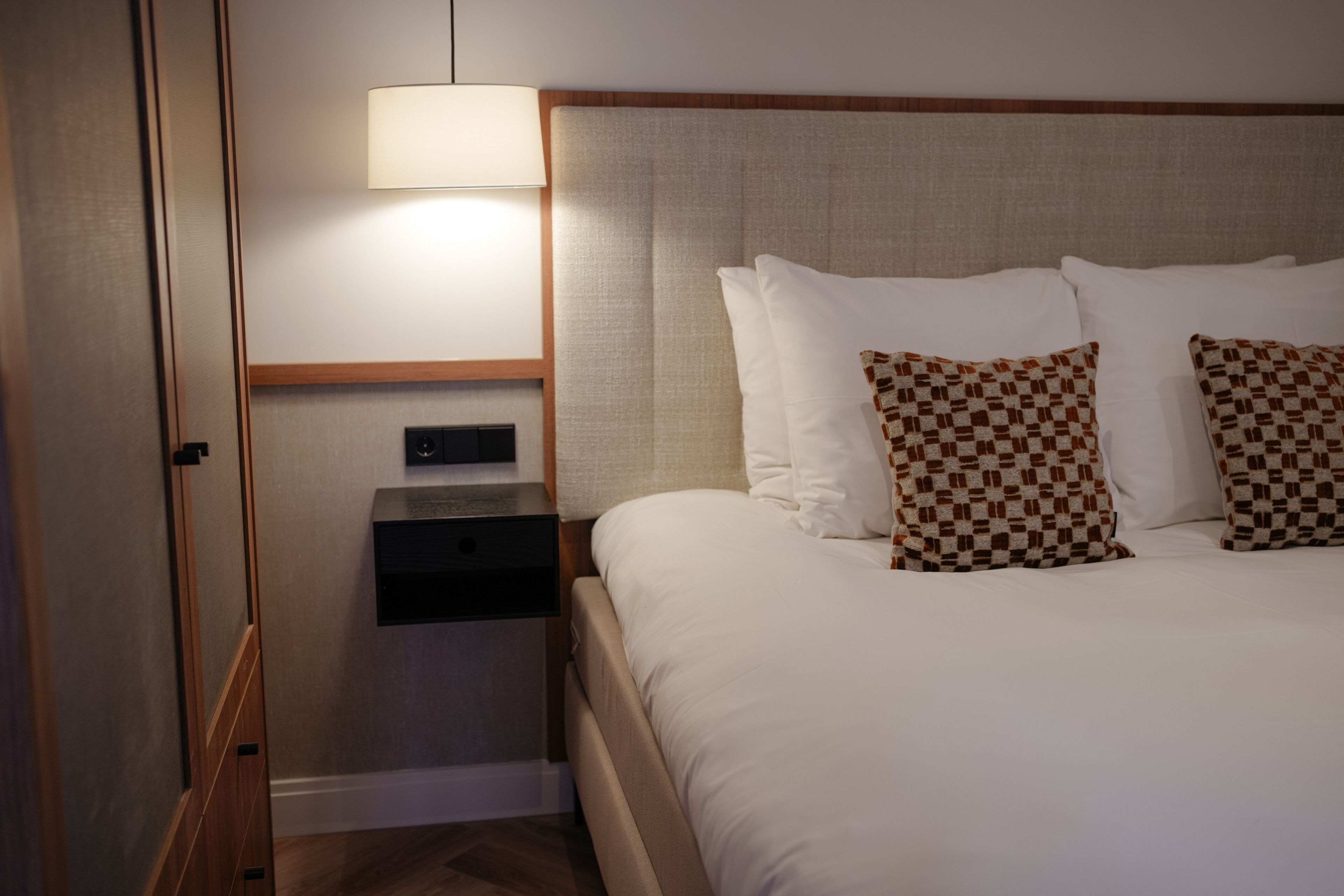 A hotel room with a bed, a nightstand, a lamp, and a wall-mounted control panel.