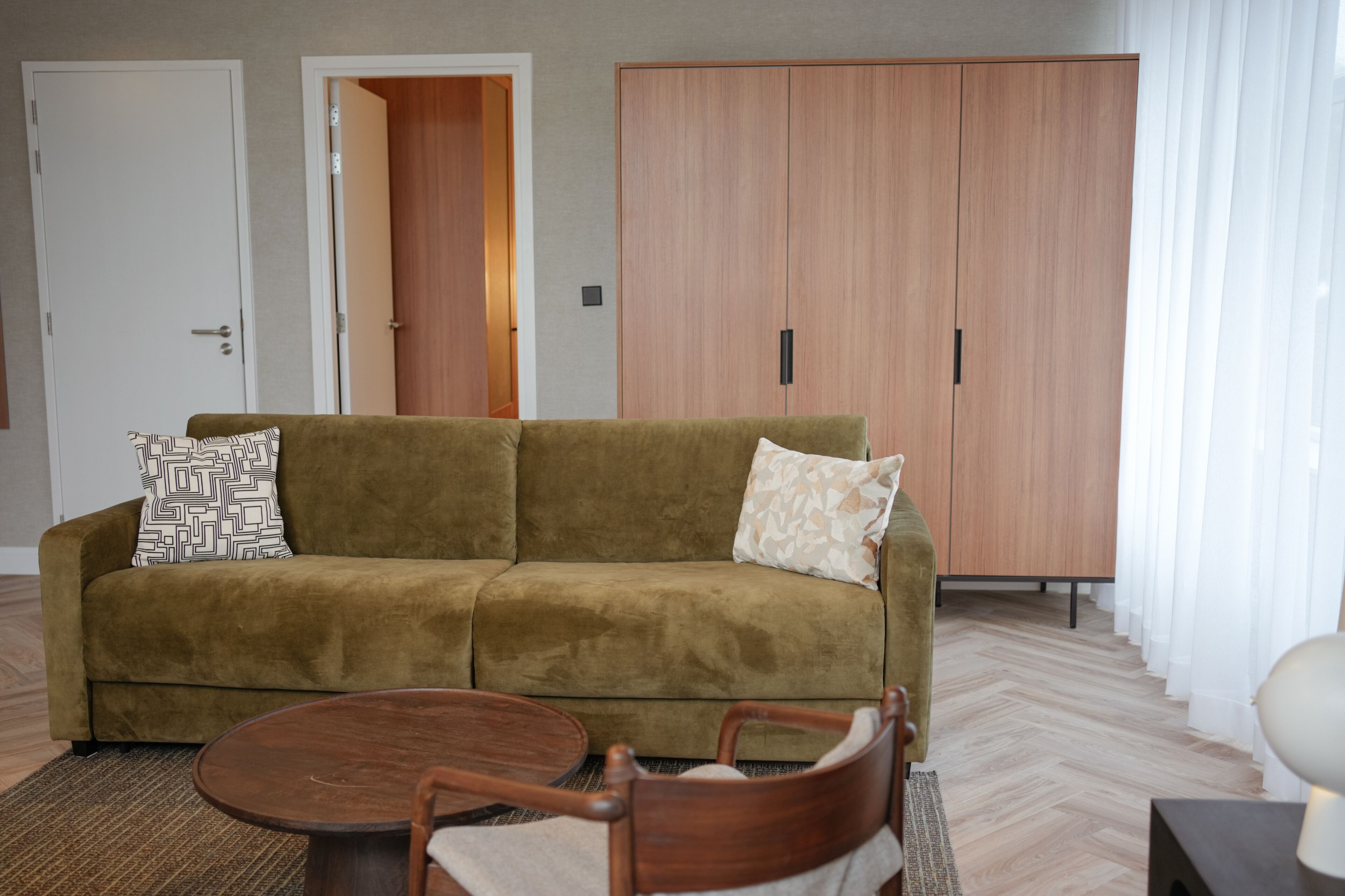 Ein Wohnzimmer mit Sofa, zwei Stühlen, einem Couchtisch, einem Kleiderschrank und einer Tür.