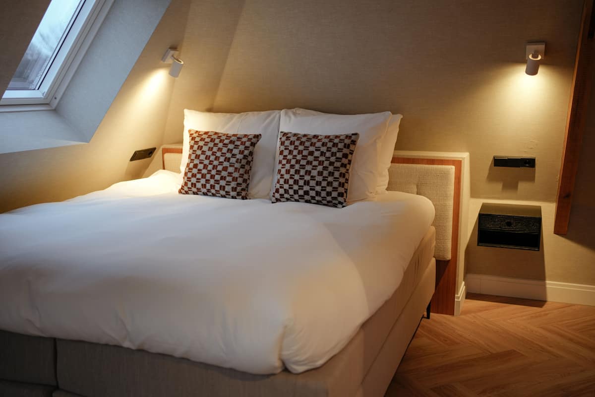 A neatly made bed with checkered pillows, a wooden headboard, and a small bedside table with a lamp.