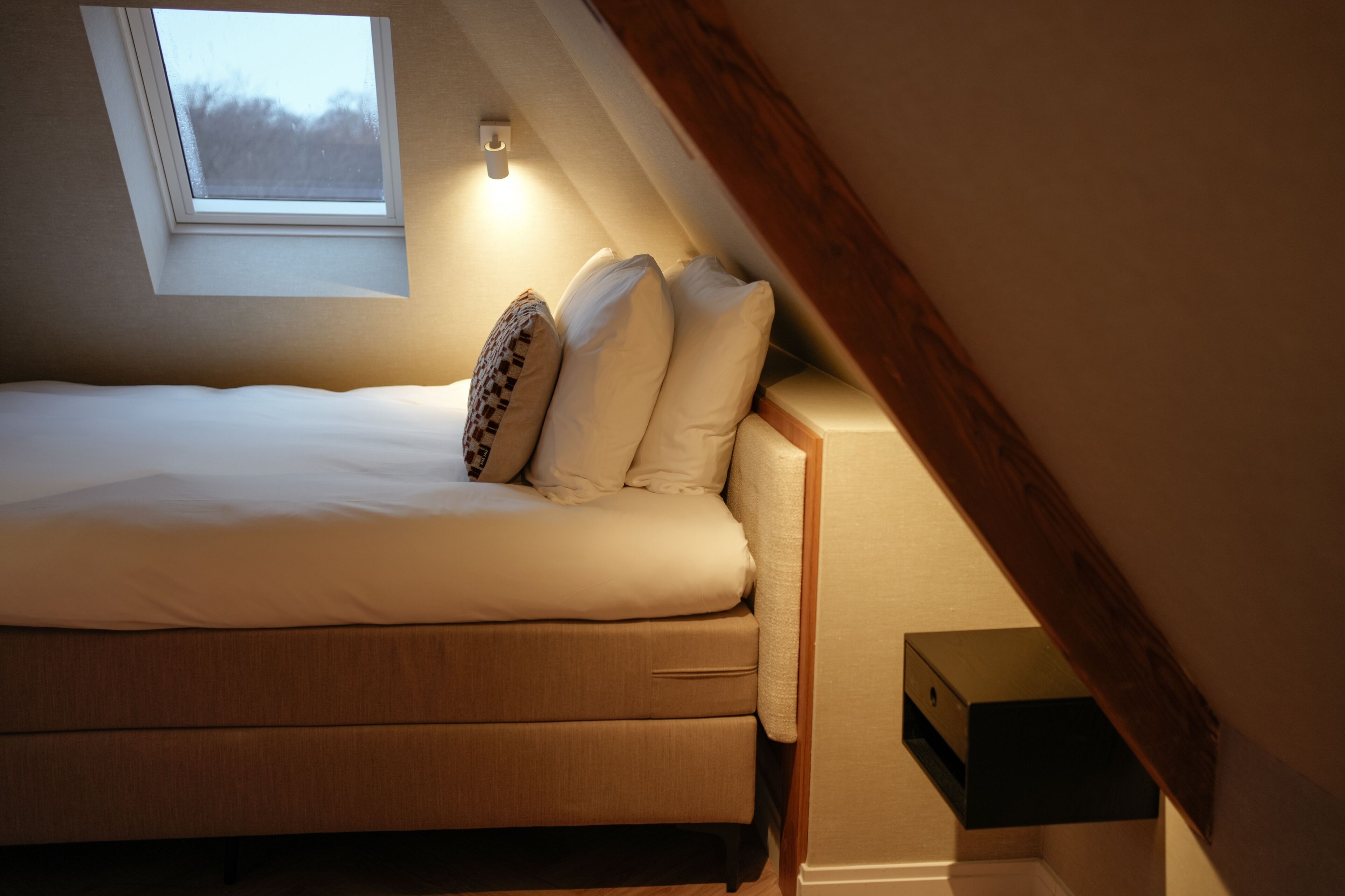 A bedroom with a bed, pillows, a nightstand, and a small window.