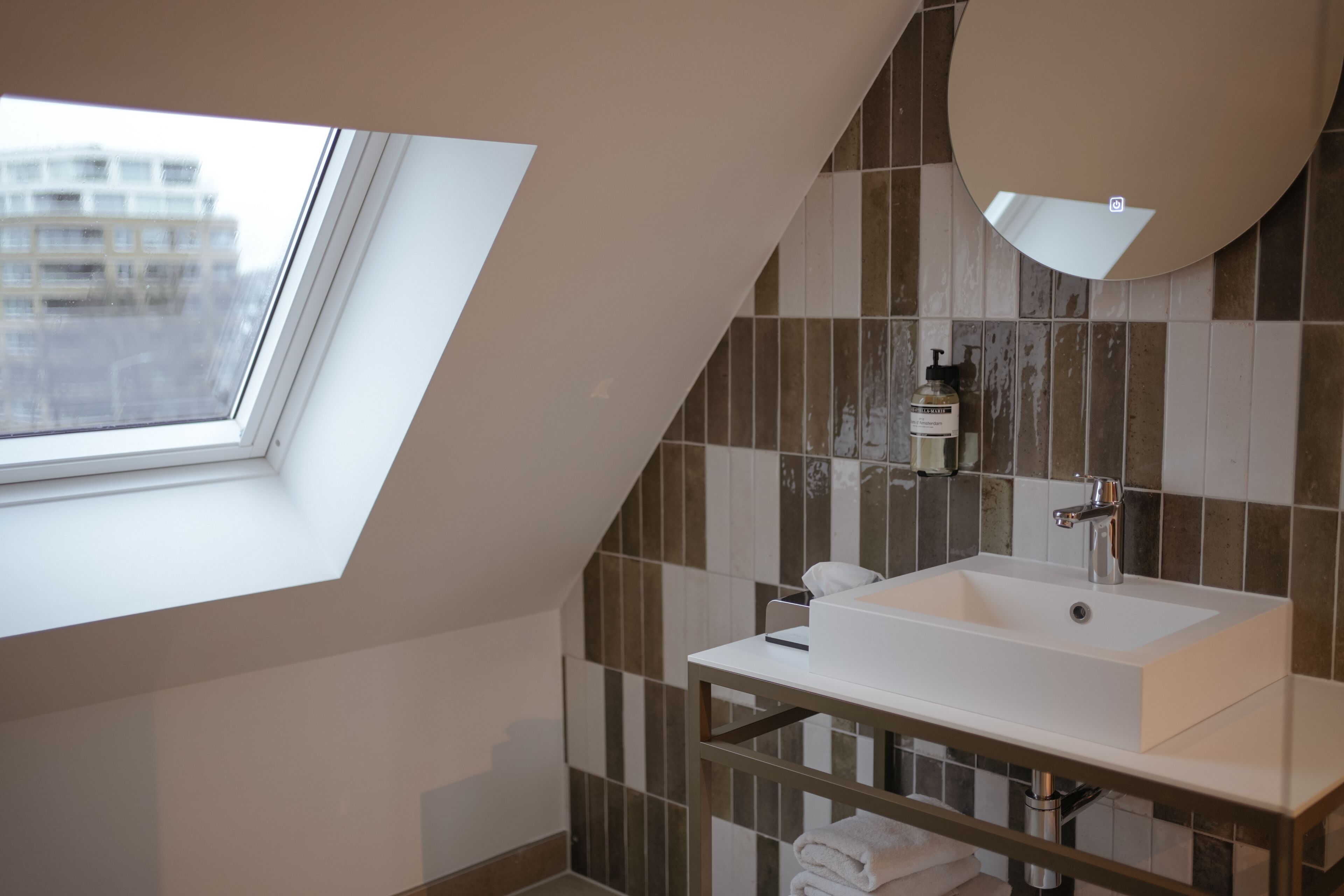 Un baño moderno con tragaluz, un espejo grande y un lavamanos blanco.