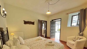 Een slaapkamer met een bed, een stoel, een nachtkastje en een deur naar een balkon.