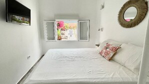 A bedroom with a bed, a window with open shutters, a mirror on the wall, and a view of greenery outside. - Eden Gomera Suite (Lepe)