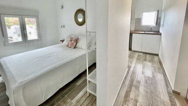 A bedroom with a bed, a small bedside table, a wall-mounted mirror, and a window with a view of the outside. - Eden Gomera Suite (Lepe)