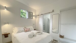 Un dormitorio con una cama grande, ducha, espejo y ventana.