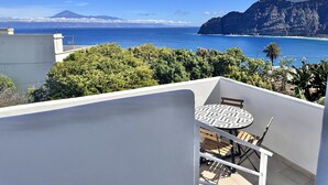 A balcony with a table and chairs, overlooking a coastal view with mountains and the sea. - Eden Gomera Suites - Rooftop terrace 2Br apartment with gorgeous oceanviews (Lepe)