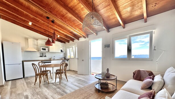 A modern kitchen with wooden beams, a dining area with a table and chairs, and a living room with a sofa and a view of the sea. - Eden Gomera Suites - Rooftop terrace 2Br apartment with gorgeous oceanviews (Lepe)