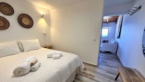 A bedroom with a large bed, a wooden bench, and a view of another room. - Eden Gomera Suites - Rooftop terrace 2Br apartment with gorgeous oceanviews (Lepe)
