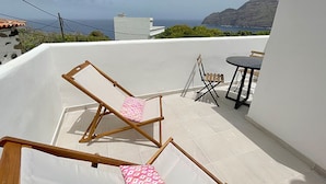 A sunlit terrace with a wooden chair and a small table, overlooking a coastal landscape. - Eden Gomera Terrace Apartment oceanviews (Lepe)
