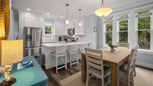 A modern kitchen with white cabinets, stainless steel appliances, and a wooden dining table. - *New* Beach Hair Don't Care, hot tub, close to pool (Pacific Beach)