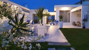 En moderne udendørs terrasse med pool, siddepladser og en velholdt græsplæne.