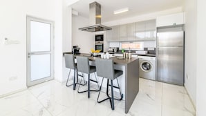 A modern kitchen with a central island, built-in appliances, and a washing machine. - Olivine Sea Pearl Villa #18 (Paralimni)