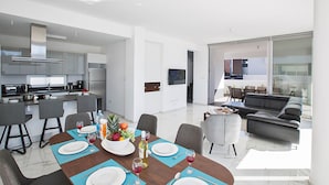 A modern living space with a dining area, kitchen, and a balcony with a sofa. - Olivine Sea Pearl Villa #18 (Paralimni)