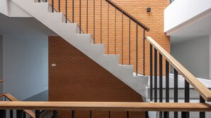 A staircase with a wooden handrail and black balusters, leading to a room with a brick wall and a white ceiling. - Chamemon Bed Phuket Town (Phuket)